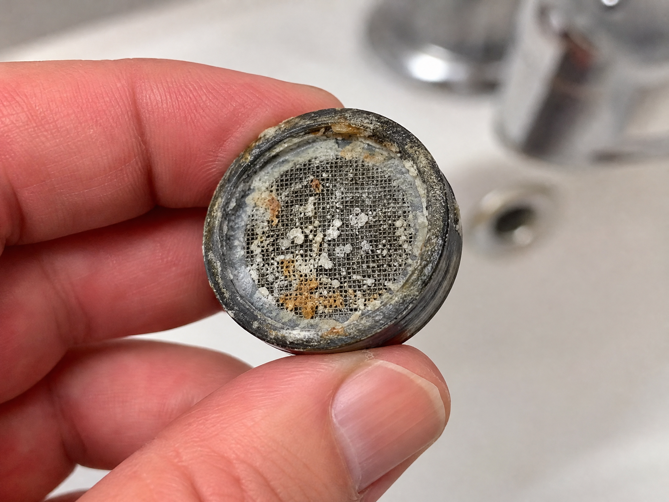 Hand holding a faucet aerator screen covered in white calcium and mineral buildup from San Antonio hard water